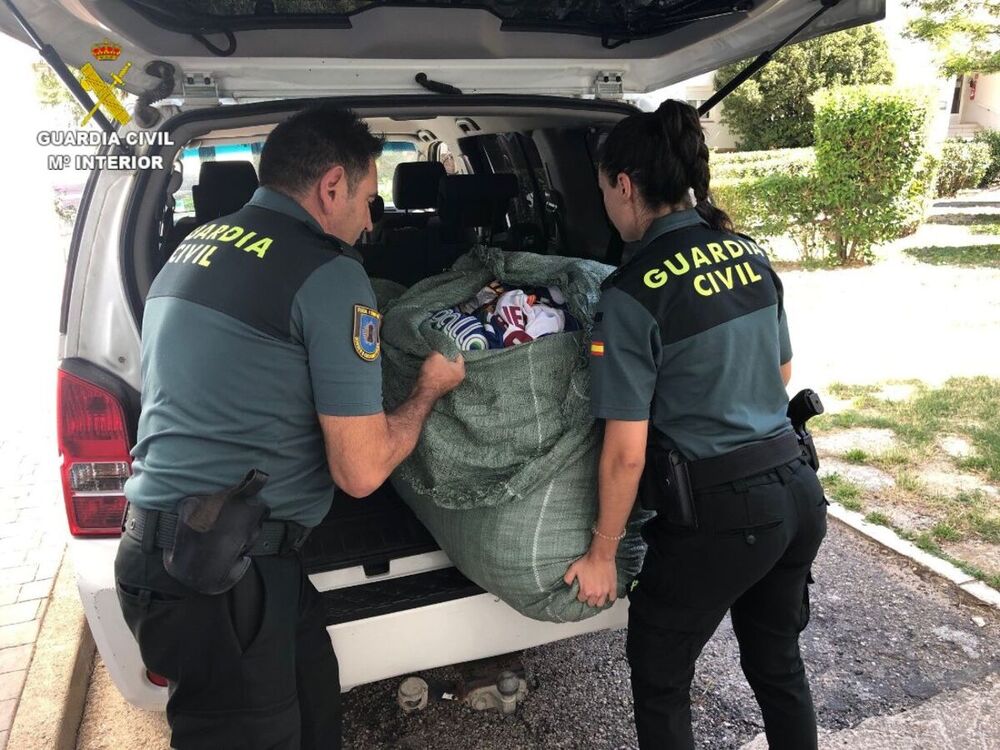 Dos agentes cargan el un vehículo un bolsa con ropa falsificada